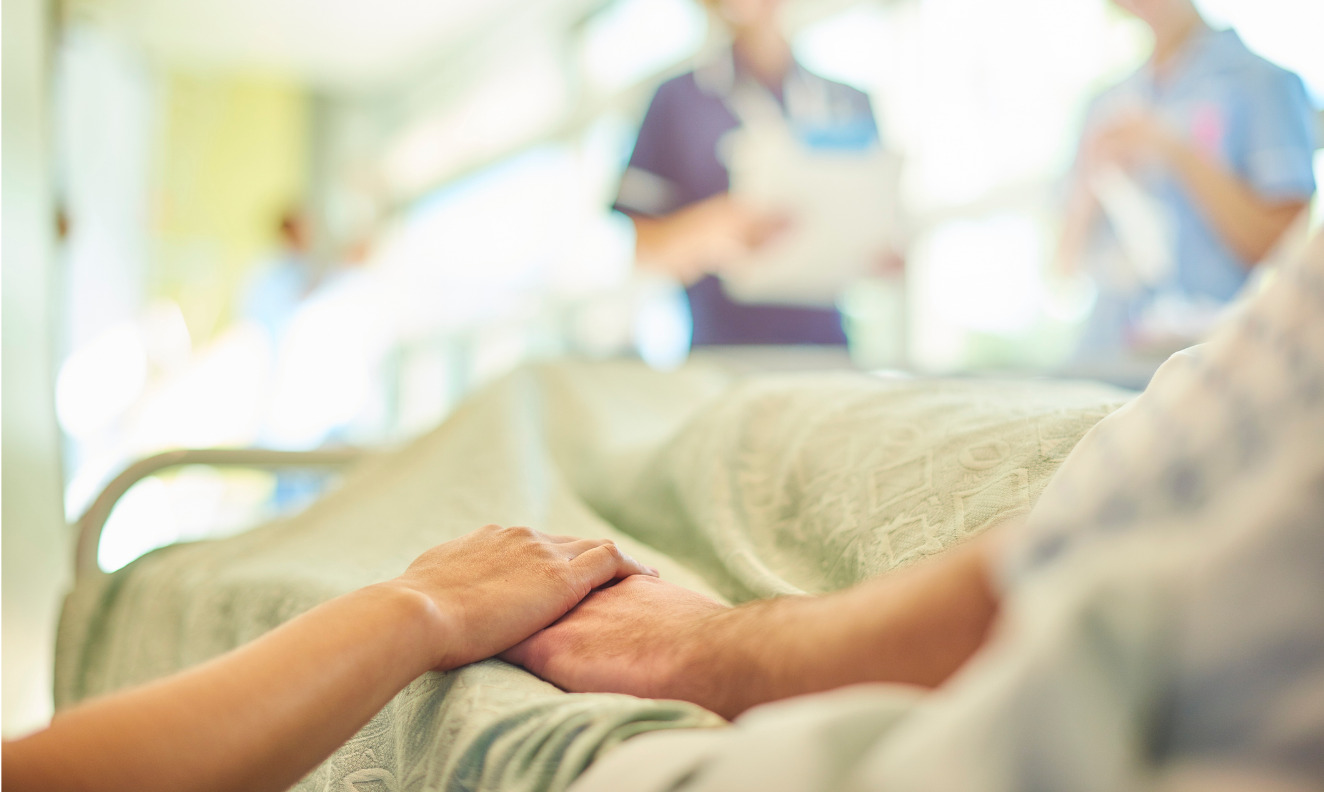 patient in a hospital bed holding hands with a visitor
