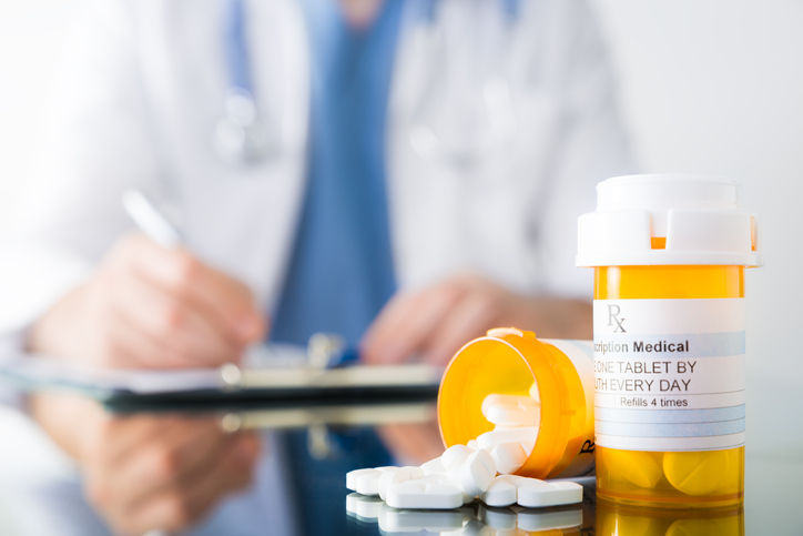doctor writing prescription with bottles of pills on table