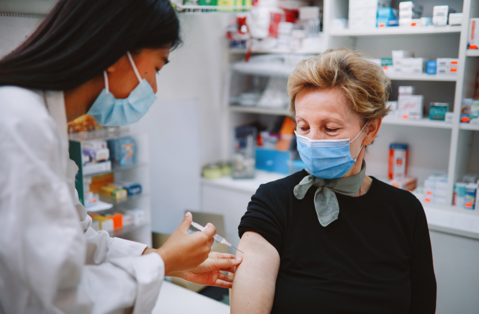 pharmacist giving a vaccination to a senior woman in a retail pharmacy setting