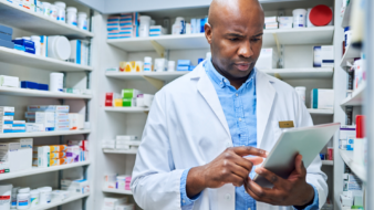 retail pharmacist working on a tablet device looking at legislative reports in the pharmacy stock room