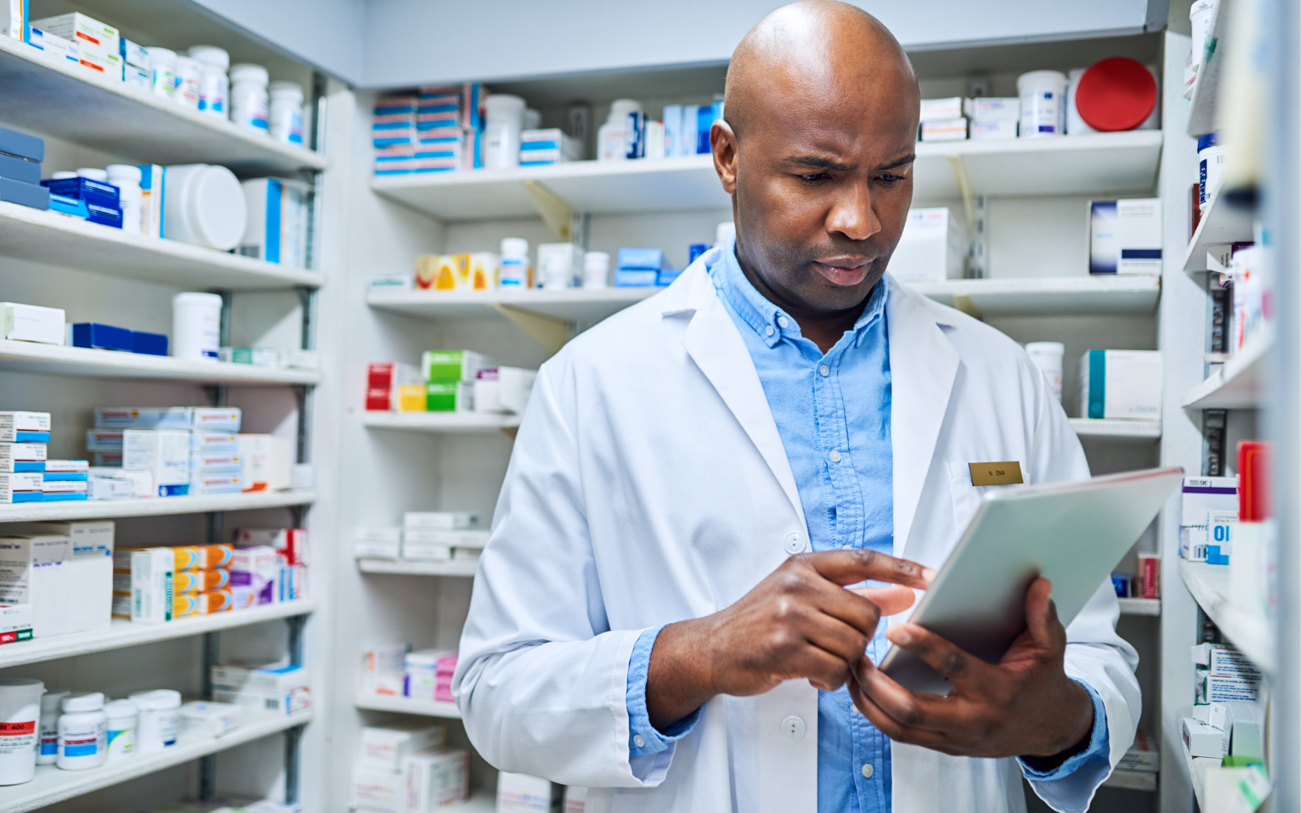 retail pharmacist working on a tablet device looking at legislative reports in the pharmacy stock room