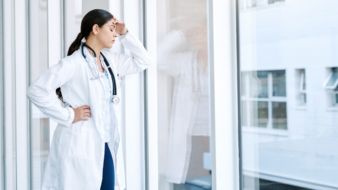 physician standing in front of a window looking stressed