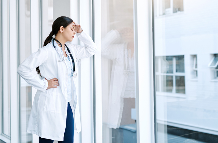 physician standing in front of a window looking stressed