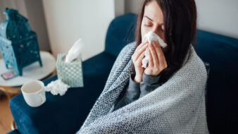 sick woman blowing her nose while sitting on the couch
