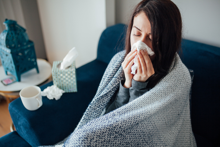 sick woman blowing her nose while sitting on the couch